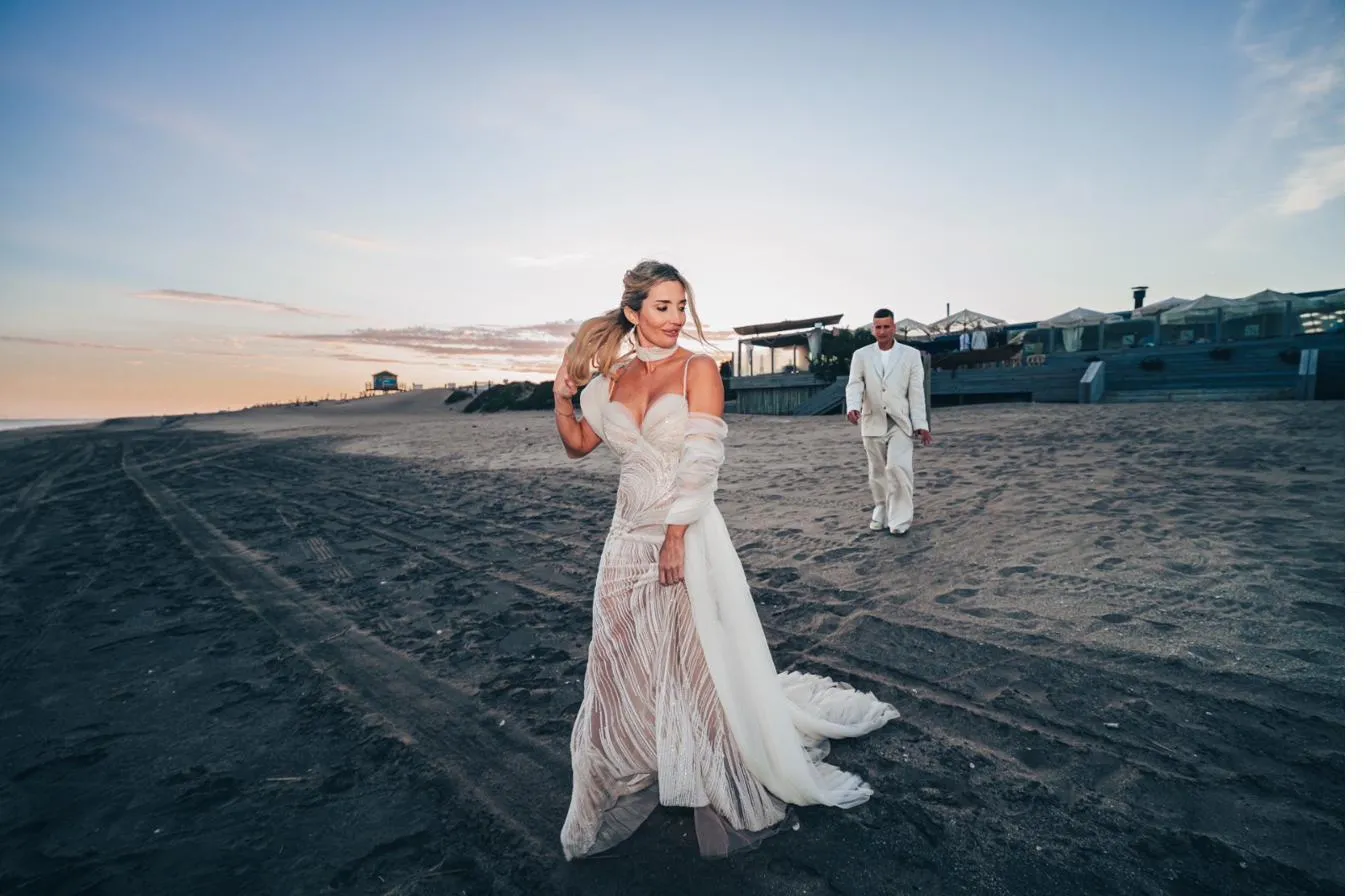 La novia caminando sobre la arena al atardecer, con el vestido al viento